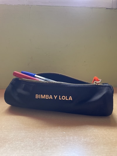 A sleek, minimalist pencil case in soft leather resting on a wooden desk with scattered pencils.