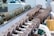 A row of metal dumbbells neatly arranged on a rack in front of a mirrored wall. The background shows gym equipment and reflections. The setting is clean and organized, emphasizing functional fitness spaces.