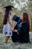 a woman in a graduation gown and cap next to a girl in a dress