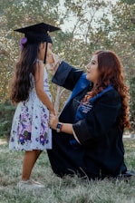 a woman in a graduation gown and cap next to a girl in a dress