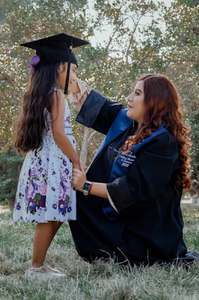 a woman in a graduation gown and cap next to a girl in a dress