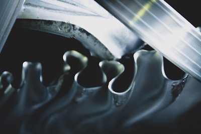 A close-up view of interlocking metallic gears with smooth, wavy edges reflecting light. The gears are intricately aligned, creating a sense of movement and precision.
