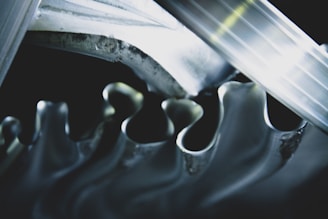 A close-up view of interlocking metallic gears with smooth, wavy edges reflecting light. The gears are intricately aligned, creating a sense of movement and precision.