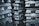 Stacks of metallic ingots, arranged in several layers, appearing shiny and rough in texture. The ingots are tightly packed, creating a pattern of repeating shapes and reflections.