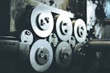 A collection of industrial machine parts featuring multiple large, circular metal components with bolts. The setting appears dimly lit, highlighting the metallic surfaces and their intricacies.