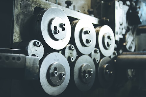 A collection of industrial machine parts featuring multiple large, circular metal components with bolts. The setting appears dimly lit, highlighting the metallic surfaces and their intricacies.