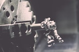 A close-up view of a metal lathe with intricate metallic curls and shavings being formed as the machine operates. The image captures the mechanical precision of the lathe's spinning, with a focus on the textures and shapes of the metal components.