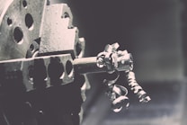A close-up view of a metal lathe with intricate metallic curls and shavings being formed as the machine operates. The image captures the mechanical precision of the lathe's spinning, with a focus on the textures and shapes of the metal components.