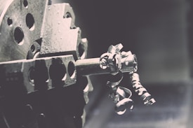 A close-up view of a metal lathe with intricate metallic curls and shavings being formed as the machine operates. The image captures the mechanical precision of the lathe's spinning, with a focus on the textures and shapes of the metal components.