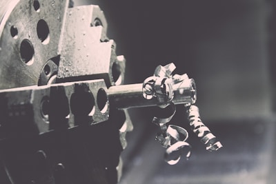 A close-up view of a metal lathe with intricate metallic curls and shavings being formed as the machine operates. The image captures the mechanical precision of the lathe's spinning, with a focus on the textures and shapes of the metal components.