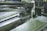 A metal-cutting machine in action, with a saw blade slicing through pipes and coolant fluid being applied to reduce heat and friction. The environment has an industrial and mechanical feel with visible metal shavings and gears.