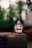 A small, transparent glass figurine of a deity sits on a textured stone surface. The background is a soft blur of greenery, which gives a natural and serene setting.