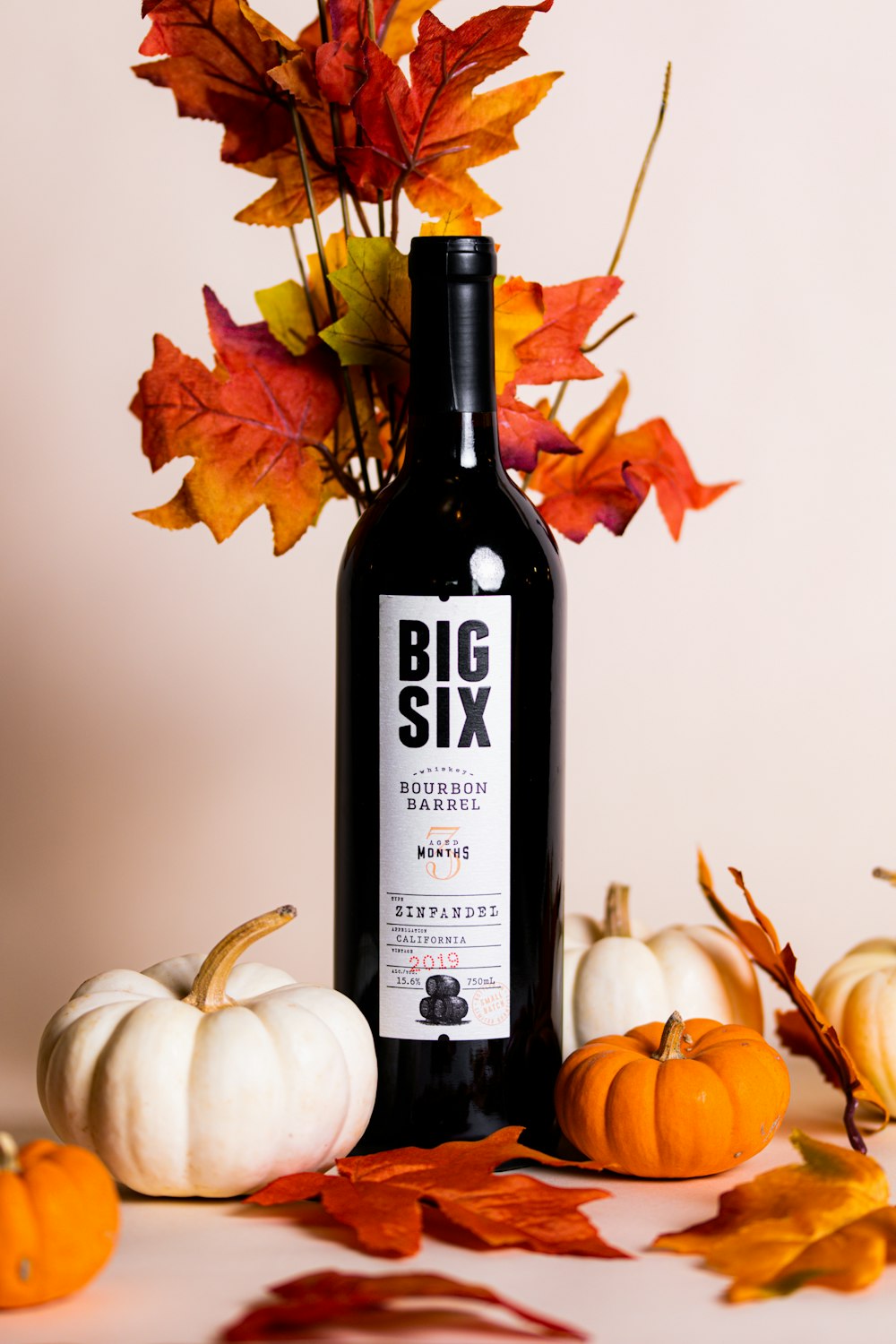 a bottle of wine next to pumpkins and a couple of pumpkins