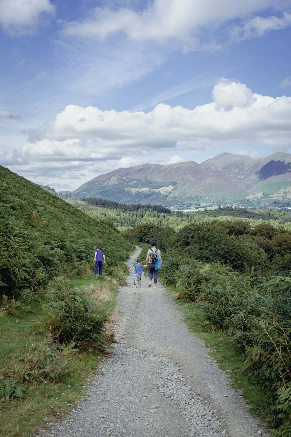 a group of people walking on a dirt road in a hilly area