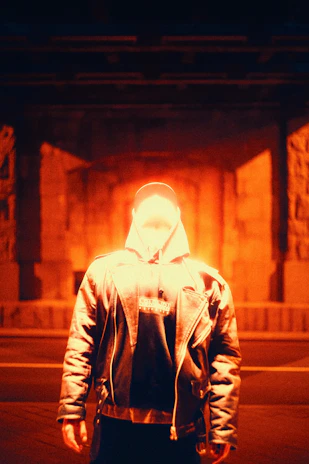 Model in urban rage bomber jacket standing under electric orange streetlights with fog swirling around.