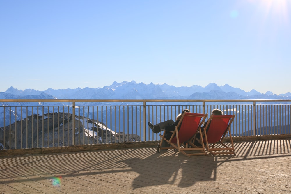 a deck with chairs and a table on it with mountains in the background