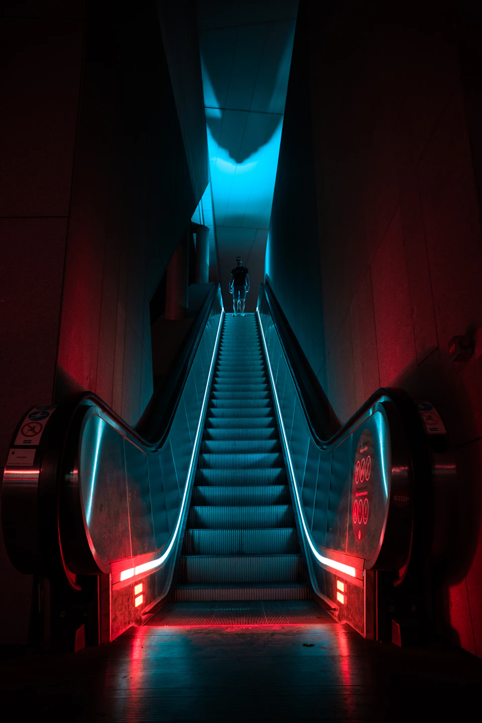 Modern escalator with blue and red lights at top, surrounded by empty white space