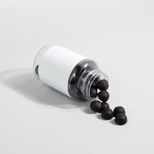 A transparent plastic bottle with a white label is lying on its side, spilling out several black sphere-shaped objects onto a light gray surface.