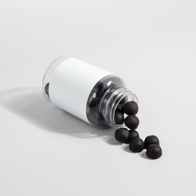 A transparent plastic bottle with a white label is lying on its side, spilling out several black sphere-shaped objects onto a light gray surface.