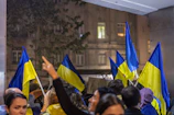 Outdoor meeting with representatives from various institutions discussing plans with blue and white flags in the background.