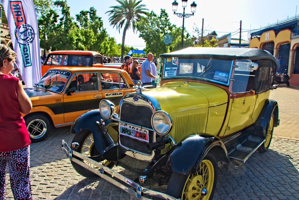 a group of people standing around a car parked on a brick road