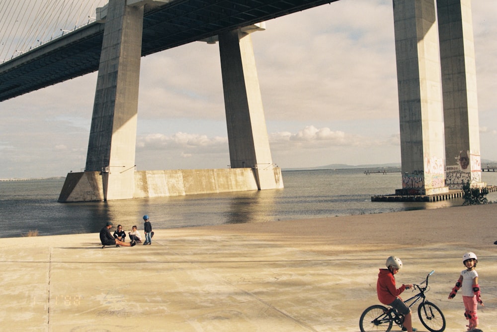 a group of people sitting on a beach under a bridge