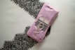 A neatly wrapped package in pink paper is tied with twine, placed on top of an elegant black lace fabric. The package includes a label that suggests a sophisticated product presentation.