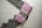 A neatly wrapped package in pink paper is tied with twine, placed on top of an elegant black lace fabric. The package includes a label that suggests a sophisticated product presentation.