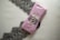A neatly wrapped package in pink paper is tied with twine, placed on top of an elegant black lace fabric. The package includes a label that suggests a sophisticated product presentation.