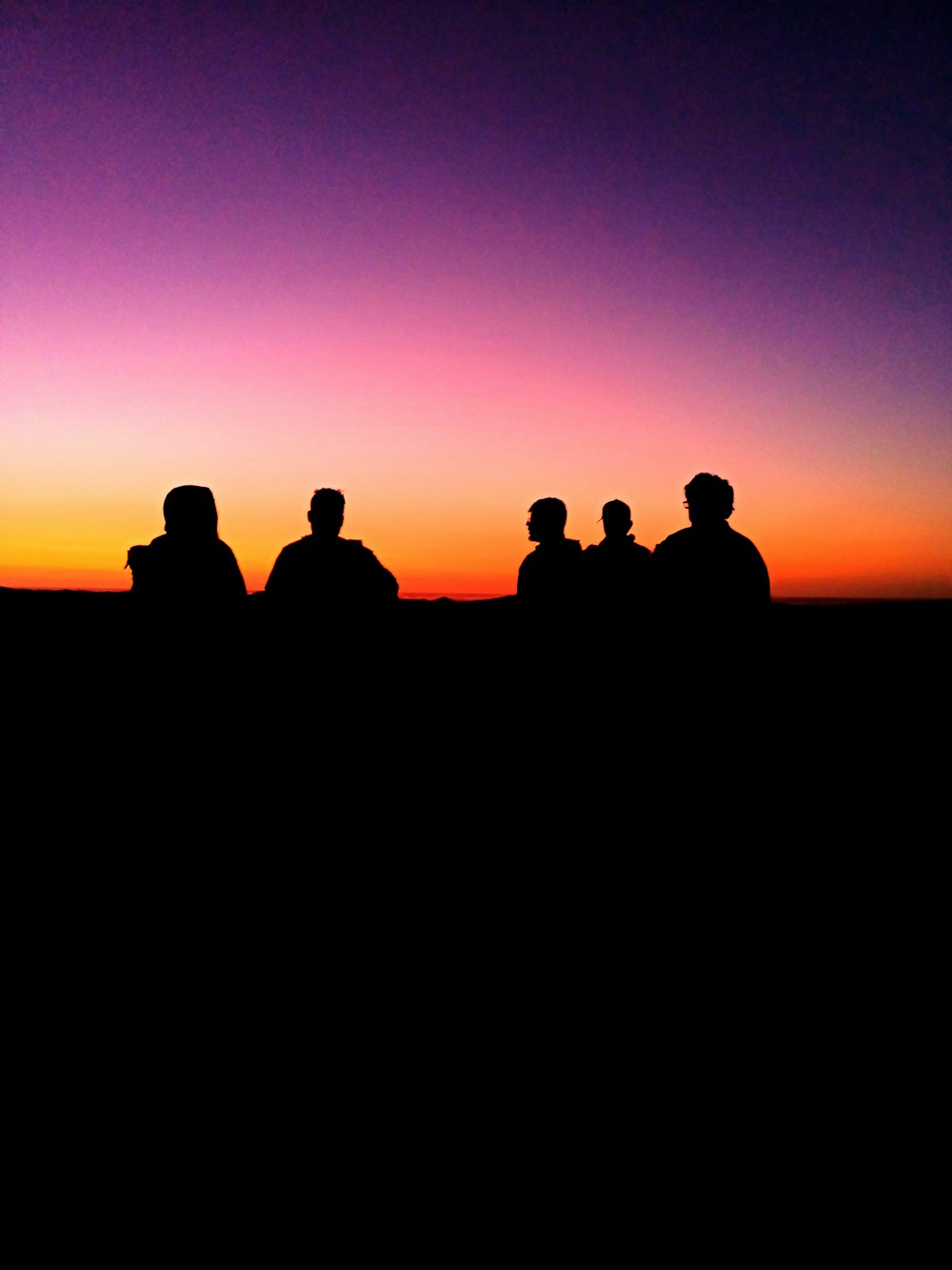 silhouette of people sitting in front of a sunset