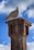 A seagull is perched atop a rusty metal post against a backdrop of a bright blue sky with scattered clouds.