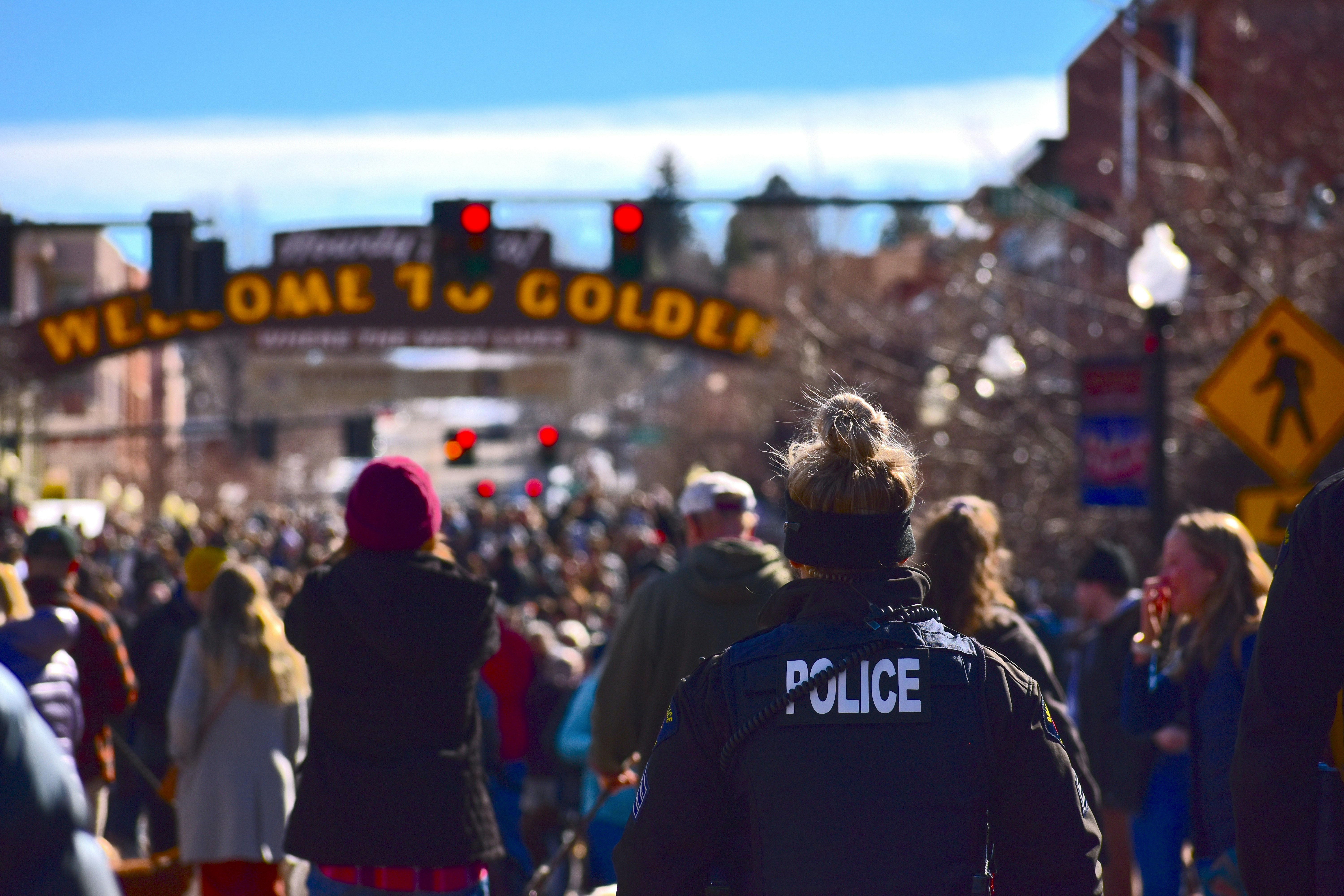 A somber, blurred photo of a crowd gathered, with police tape visible in the background, symbolizing a crime scene and public concern.