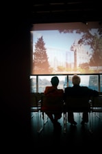 A couple watching a large screen displaying a vibrant multimedia presentation in a cozy room.