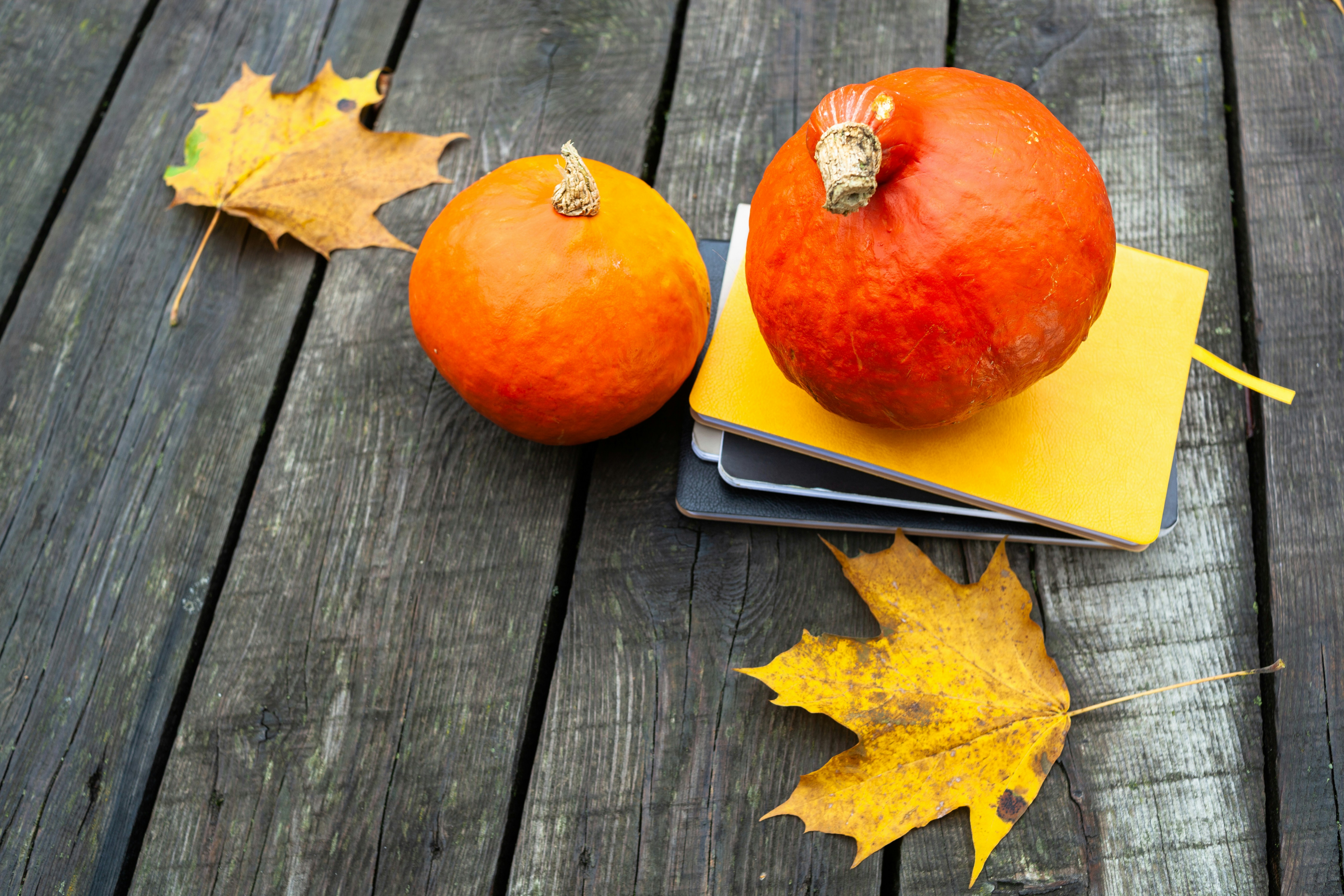 a couple of pumpkins on a cutting board with a yellow plate and a leaf on a wood