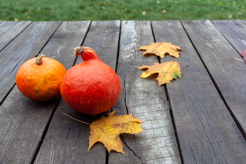 a couple of tomatoes on a wood surface with leaves