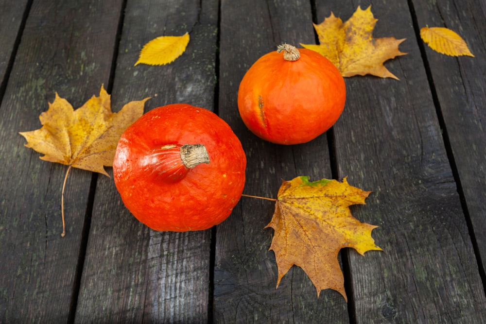 a couple of pumpkins on a wood surface with leaves