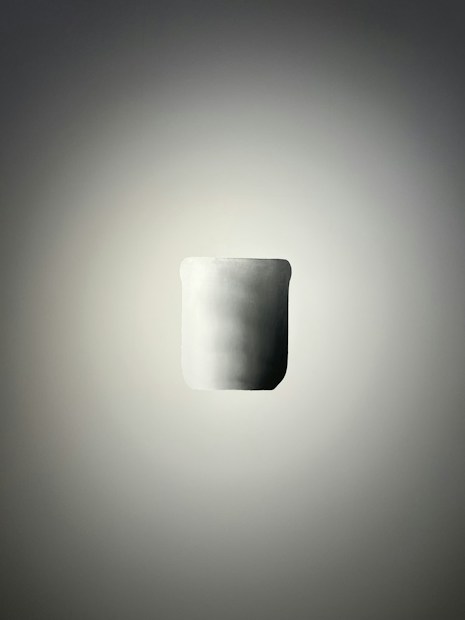 A minimalist, smooth cylindrical object with a matte finish is positioned centrally against a soft gradient background. The lighting creates a subtle shadow around the object, enhancing its three-dimensional appearance.