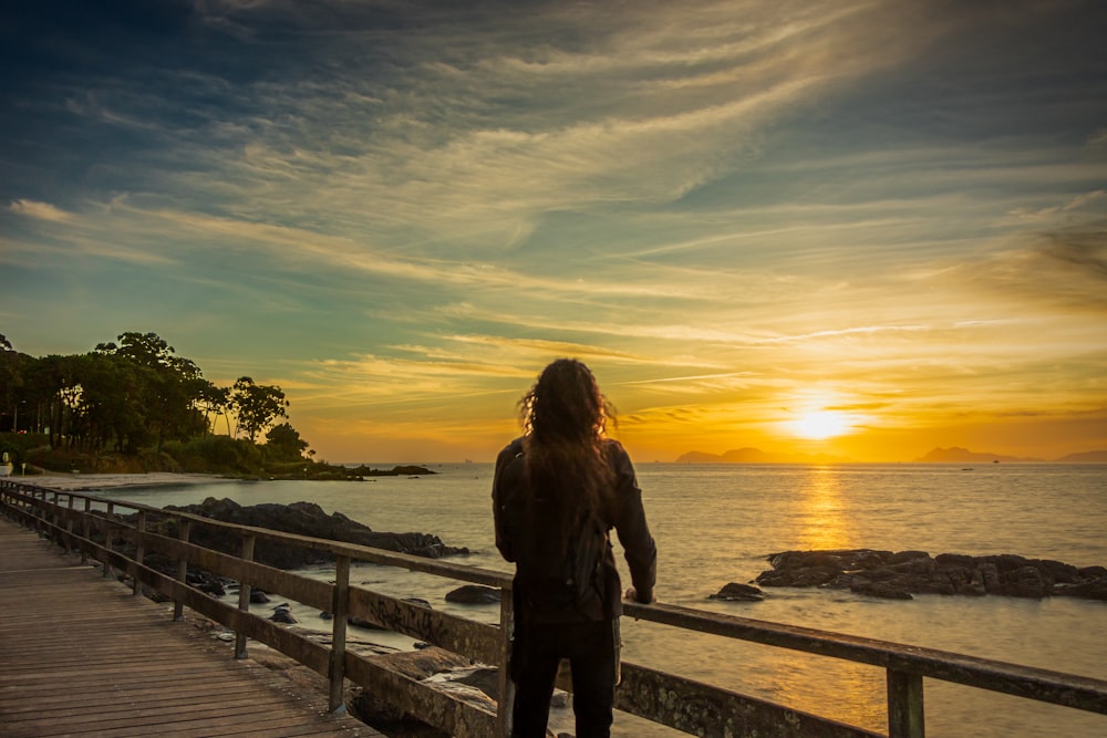 a person standing on a dock looking at the sunset