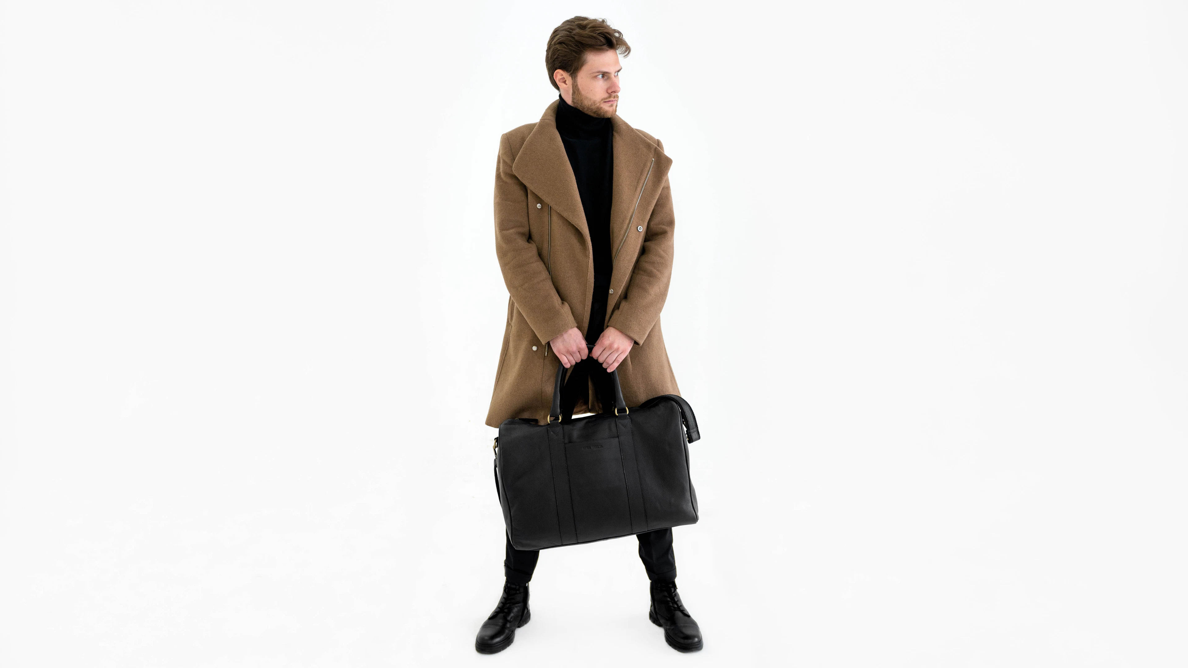 A man in a camel double-breasted coat carrying a black leather holdall