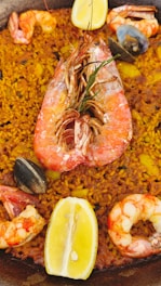 A close-up view of a seafood paella dish with yellow rice, large shrimp, mussels, and slices of lemon. The dish is rich in color and texture, featuring various seafood elements prominently placed on top of the seasoned rice.
