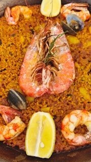 A close-up view of a seafood paella dish with yellow rice, large shrimp, mussels, and slices of lemon. The dish is rich in color and texture, featuring various seafood elements prominently placed on top of the seasoned rice.