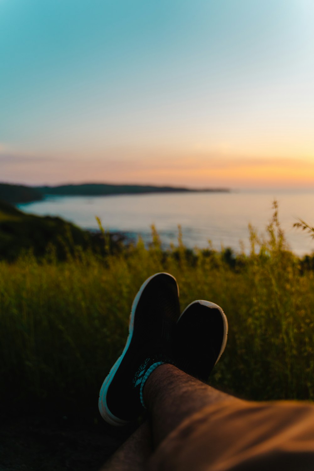 a person's feet in a grassy field with a body of water in the background