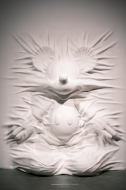 A textured wall sculpture features a prominent cartoon character with large round ears, a button nose, and gloved hands emerging from the surface. The material creates a flowing, fabric-like effect, adding depth and movement to the image.