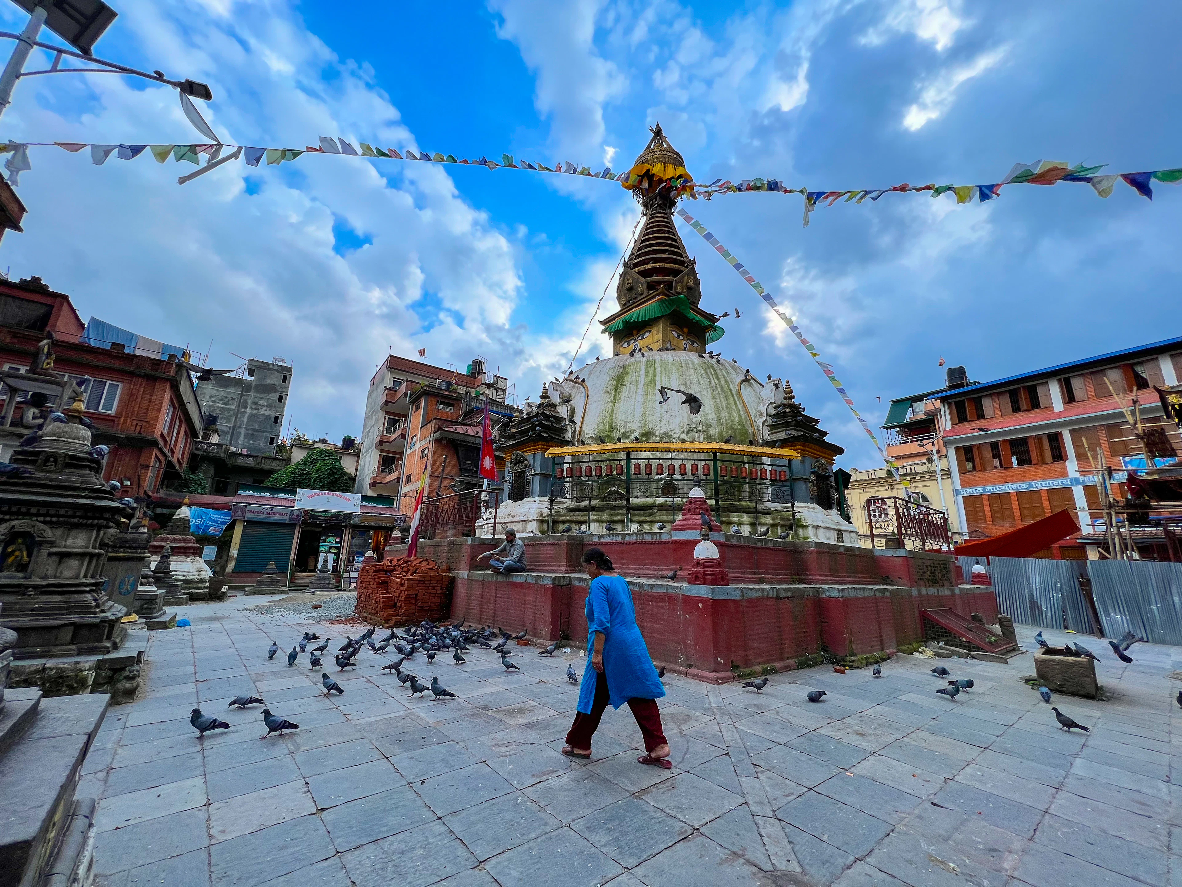 The stupa at Swayambhunath above Kathmandu, prayer flags strung over the courtyard and pigeons on the paving