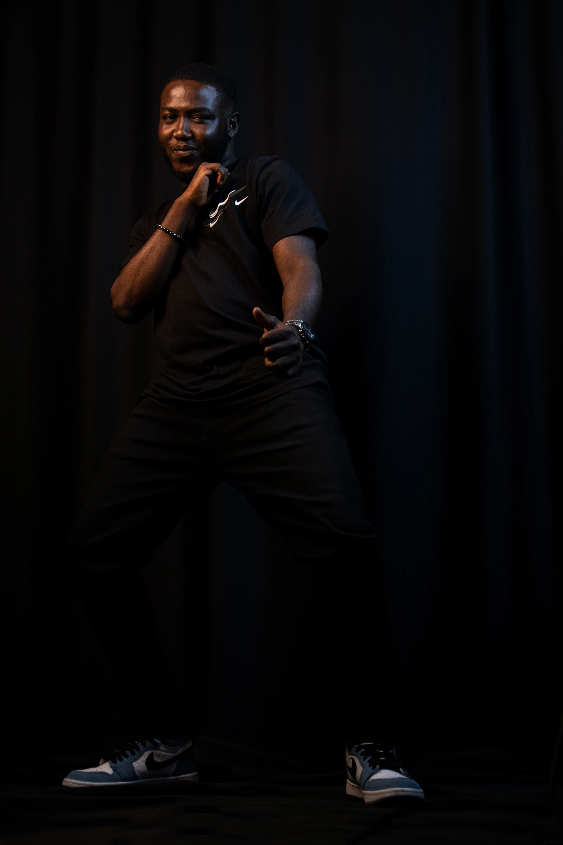A stylish model wearing a black hoodie and trousers from adidas, posed against a dark minimalist backdrop that enhances the outfit's modern luxury vibe.