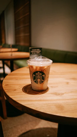 Happy customer holding a coffee tumbler while sitting at a cozy café table.