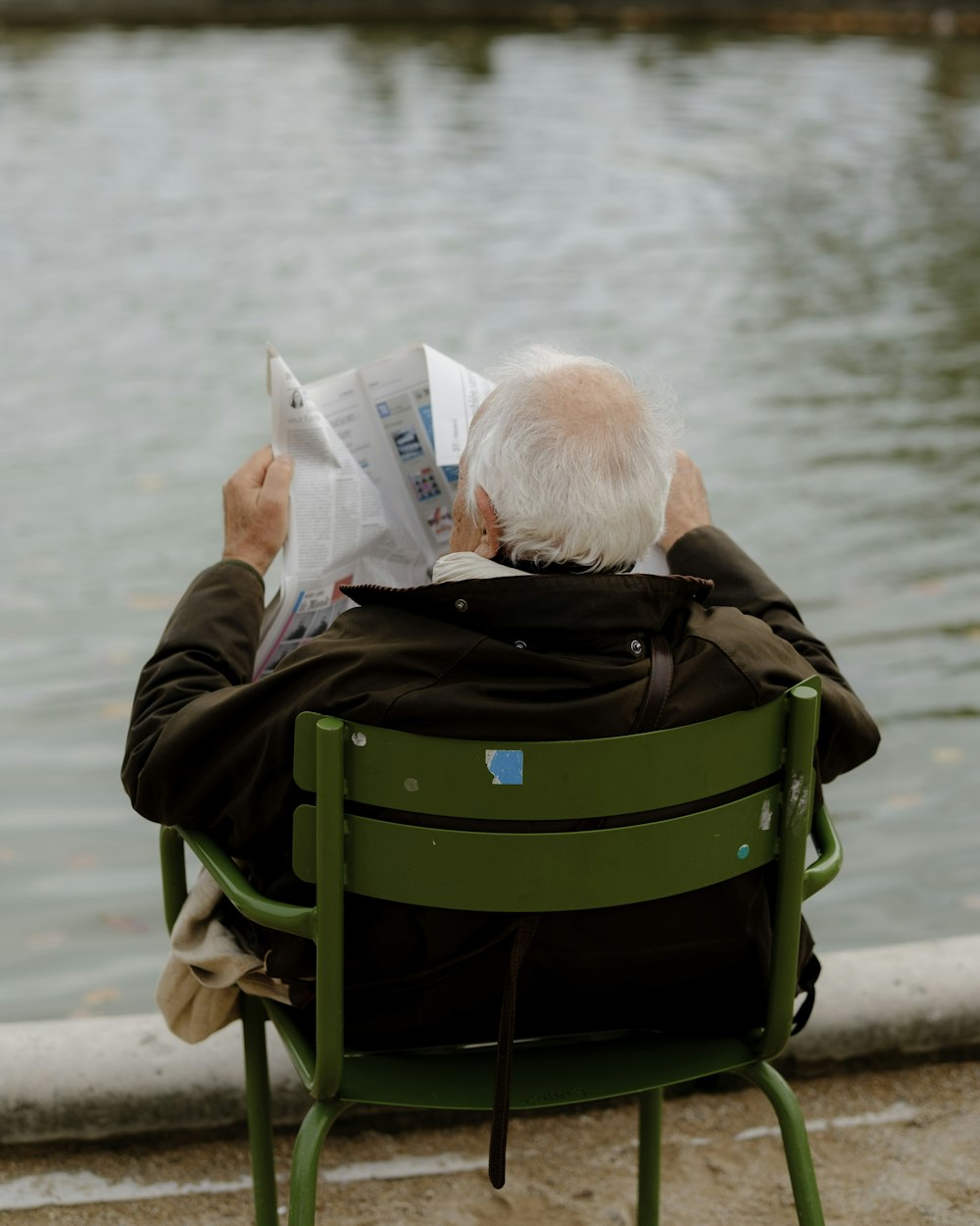 a person reading a newspaper on a bench by the water