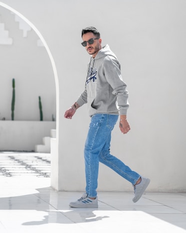 Model wearing a modern, minimalist hoodie walking through a city park in soft afternoon light
