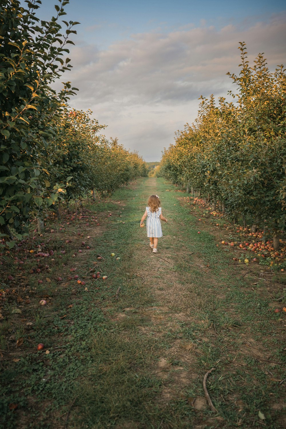 a girl walking on a path in a field of grass and trees