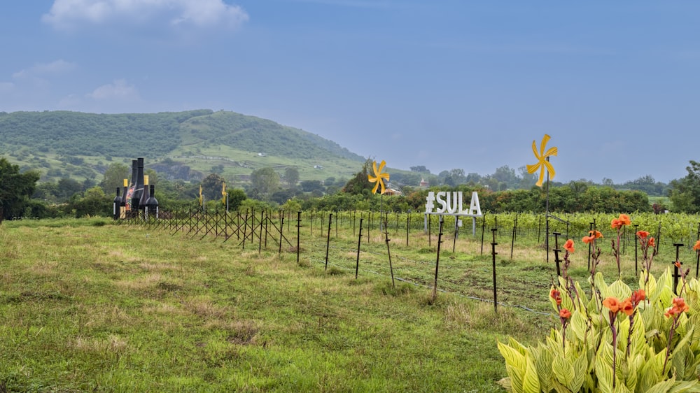 a fenced in field with a sign and flowers and hills in the background